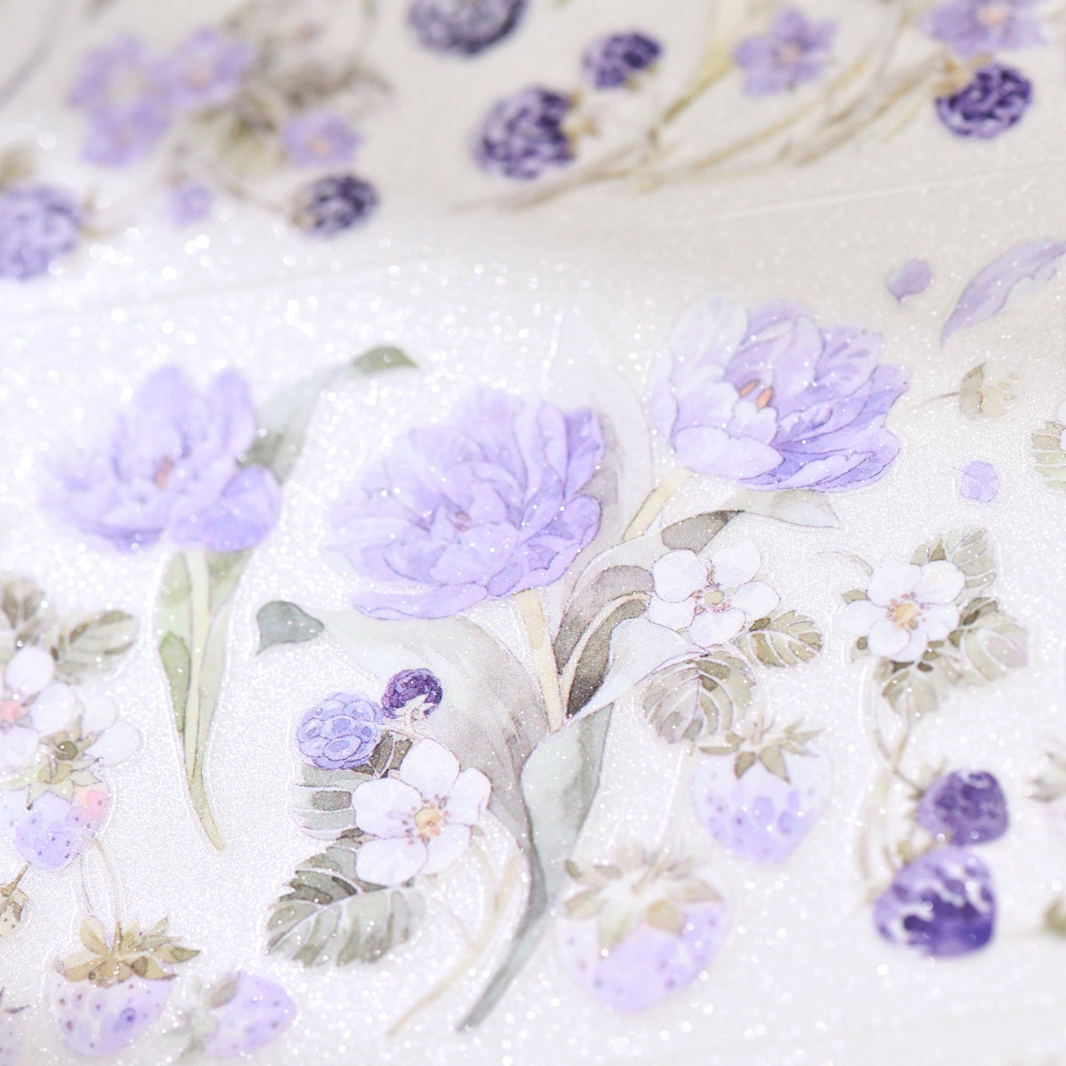 Macro close-up of Bramble Periwinkle Blue Glitter Sand PET die-cut tape with textured glitter grain and layered blue blossom petals on white background