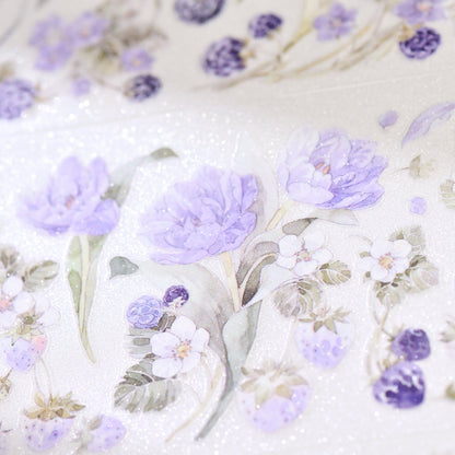 Macro close-up of Bramble Periwinkle Blue Glitter Sand PET die-cut tape with textured glitter grain and layered blue blossom petals on white background