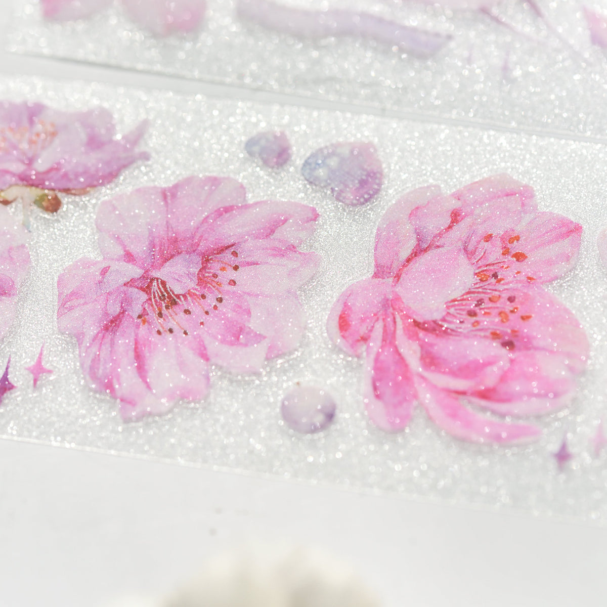 Macro close-up of Cherry Blossom Glitter Sand PET die-cut tape with textured glitter grain and delicate pink sakura petals on white background