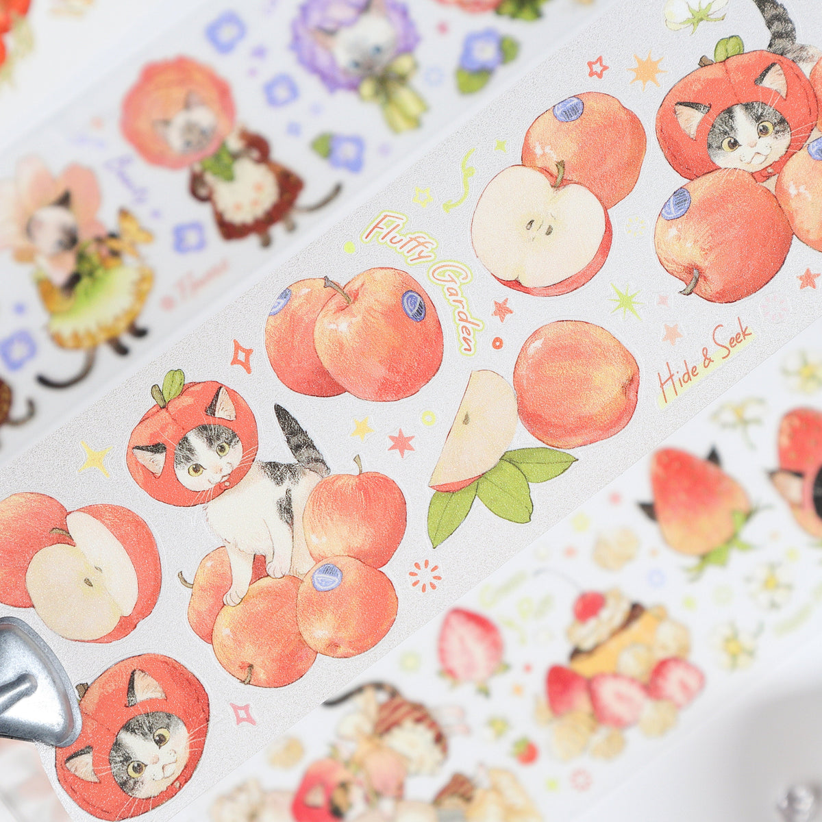 Handheld macro of Watercolor Cute Kittens Sweet Orchard Wildflower Fairy PET tape with muted coral pink watercolor cats, orchard florals and fairy accents, sparkling glitter texture and journal elements styled in the background