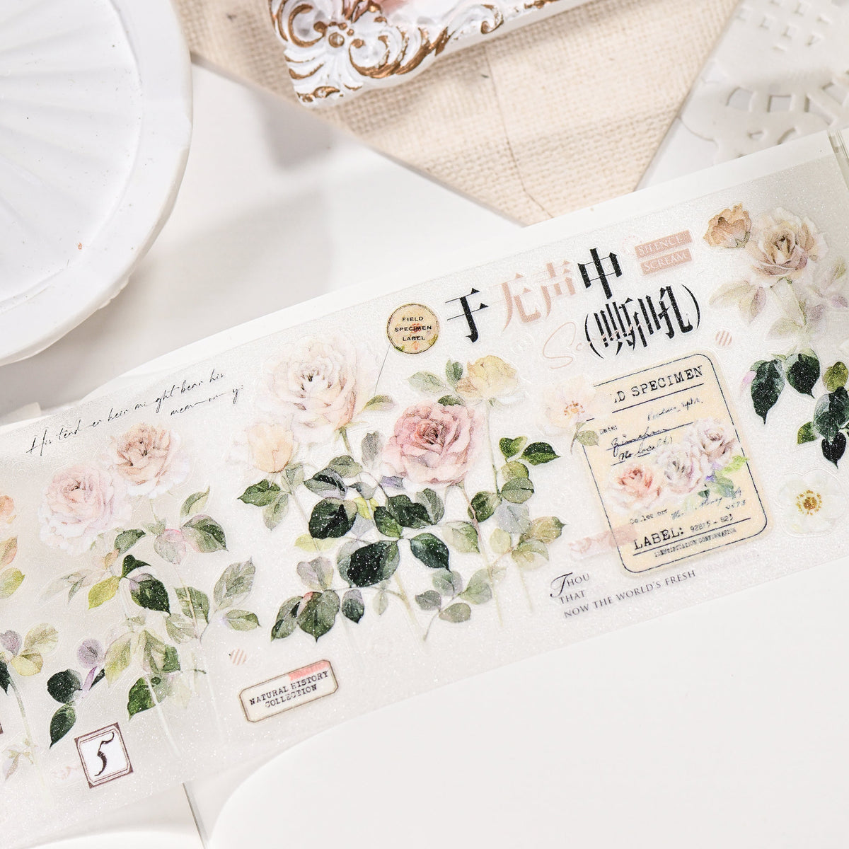 Close-up of Wilderness Rose Glacial Red Glitter Sand PET die-cut tape die-cut edges with sandy sparkle finish and champagne rose motifs in a styled flat lay
